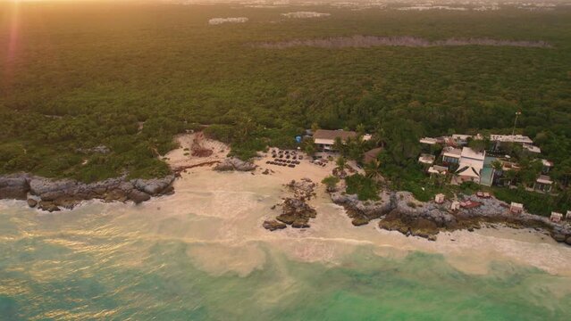 Aerial orbiting shot of Gitano Beach Club with sandy beach and Caribbean Sea at golden sunset in Mexico