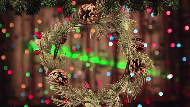 Christmas wreath with cones on a background of twinkling lights. New Year's multi-colored garlands in defocus. Holiday card with bokeh. Abstract background for captions and text. UHD 4K.
