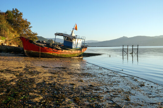 Antiguo barco de pesca varado en una playa al borde del mar. Ría de Vigo, Galicia, España.