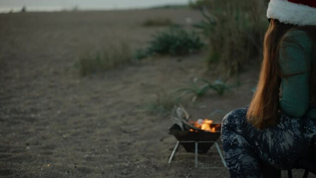 A girl in a New Year's red hat, frying marshmallows on the beach by the sea.
