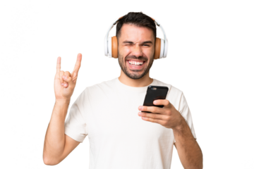 Young caucasian man over isolated chroma key background listening music with a mobile making rock gesture