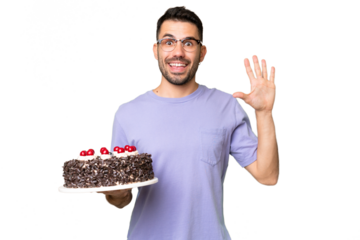 Young caucasian man holding birthday cake isolated on green chrome background saluting with hand with happy expression
