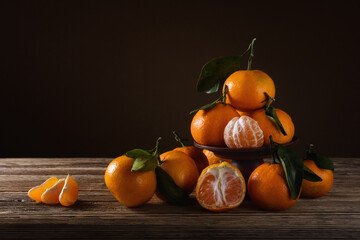 ripe orange tangerines with leaves lie on a table and a clay stand on a soft background on an old wooden table. side view with copy space and selective focus