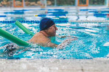 Additional swimming equipment. Side view of an elderly white man in a swimming cup, using green pool noodle. Active seniors. High quality photo