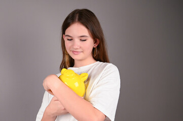 Teenage girl holding yellow piggy bank. Young girl with yellow piggy bank on gray. Save money and financial investment