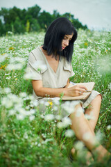 Female woman with pen writing or painting, handwriting on notebook on flower blooming meadow