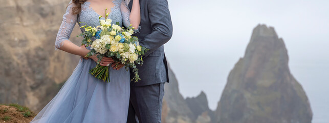 a couple standing in an embrace holding a beautiful bouquet of flowers, a girl dressed in a blue...