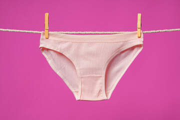 Female panties hanging on rope against pink studio background - obrazy, fototapety, plakaty