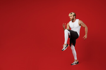 Fototapeta na wymiar Full body side profile view young strong sporty toned sportsman man wearing white clothes spend time in home gym prepare to run start isolated on plain red background. Workout sport fit body concept.