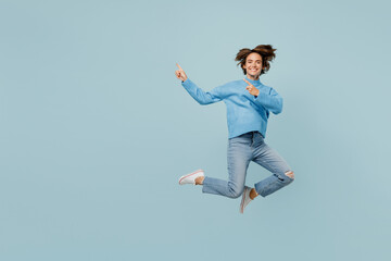 Fototapeta na wymiar Full body young woman in knitted sweater look camera jump high point index fingers aside on workspace area mock up isolated on plain pastel light blue cyan background studio People lifestyle concept