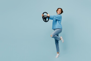 Full body young smiling cheerful fun woman in knitted sweater look camera hold steering wheel...