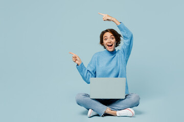 Full body young IT woman in knitted sweater hold use work on laptop pc computer point finger aside...