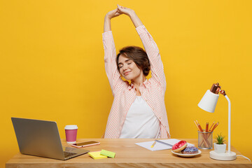 Young employee business woman in casual shirt sit work at white desk with pc laptop raise up stretch hands take break rest relax isolated on plain yellow color background Achievement career concept