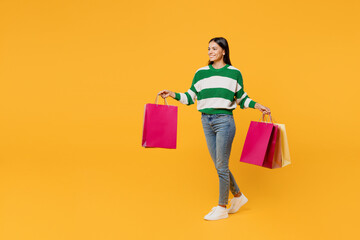 Full body young latin womanwear casual cozy green knitted sweater hold in hand paper package bags after shopping walk go isolated on plain yellow background studio. Black Friday sale buy day concept.