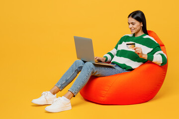 Full body young latin woman wears green sweater sit in bag chair using laptop pc computer hold...