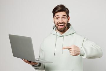 Young surprised amazed shocked caucasian man wear mint hoody hold use work point index finger on...