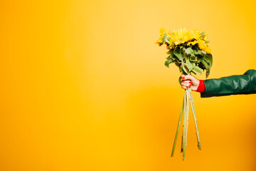 Hands of a senior woman holding a sunflower bouquet over a yellow background