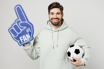 Young smiling fun man fan wear mint hoody foam 1 fan glove finger up cheer up support football...