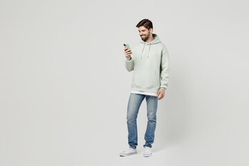 Full body young smiling happy fun cheerful cool caucasian man wearing mint hoody hold in hand use...