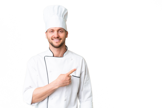 Young caucasian chef over isolated chroma key background pointing to the side to present a product