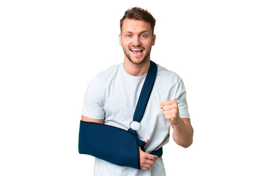 Young caucasian man with broken arm and wearing a sling over isolated chroma key background celebrating a victory in winner position