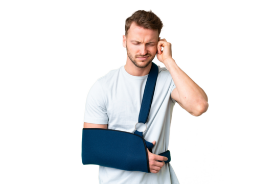 Young caucasian man with broken arm and wearing a sling over isolated chroma key background frustrated and covering ears