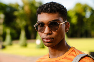 Young black man wearing piercing and sunglasses walking in park