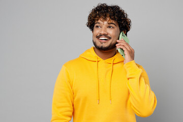 Young Indian man 20s wear casual yellow hoody talk speak on mobile cell phone conducting pleasant...