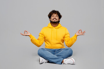 Full body spiritual young Indian man 20s he wear casual yellow hoody sit hold spreading hands in...
