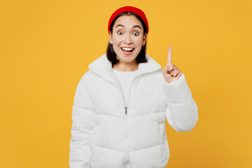 Young insighted woman of Asian ethnicity wear white padded windbreaker jacket red hat holding index finger up with great new idea isolated on plain yellow background studio. People lifestyle concept. © ViDi Studio