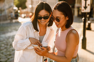 Two young beautiful smiling stylish asian girls looking at phone