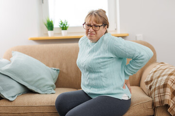 Senior woman suffering from back pain on sofa at home