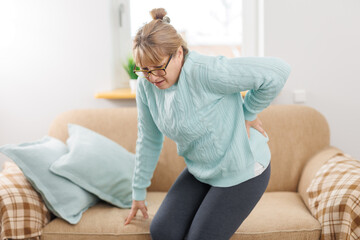 Fototapeta na wymiar Senior woman suffering from back pain on sofa at home