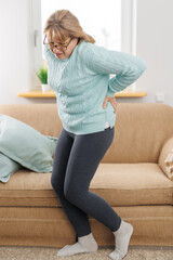 Senior woman suffering from back pain on sofa at home