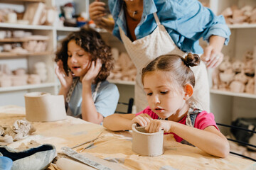 Cute kids sculpting clay crafts at table in pottery class