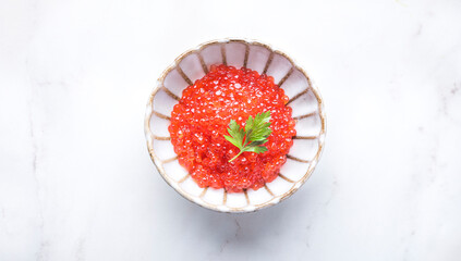 Red caviar in a beautiful ceramic bowl in the form of a flower with a silver spoon on a white  marble background. Seafood delicacies, ingredient of  Japanese cuisine