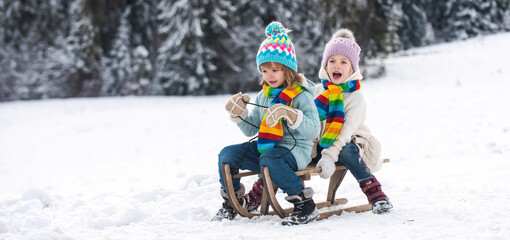 Kids ride on a wooden retro sled on a winter day. Active winter outdoors games. Friends children boy and girl sledding in winter. Kids sibling riding on snow slides in winter.