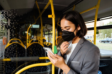 Obraz na płótnie Canvas Woman in medical mask standing in public bus with a smartphone in her hands