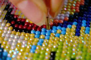 Diamond painting with pen closeup. art therapy concept. Laying out a diamond mosaic improves a woman's mental health. It calms and helps to cope with internal tension, worries and anxiety.