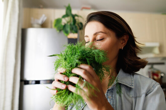Mature woman smelling dill leaves at home