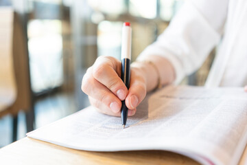 Hand of businesswoman marking in magazine with pen at cafe