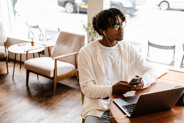 Young african american man using laptop and cellphone in cafe indoors