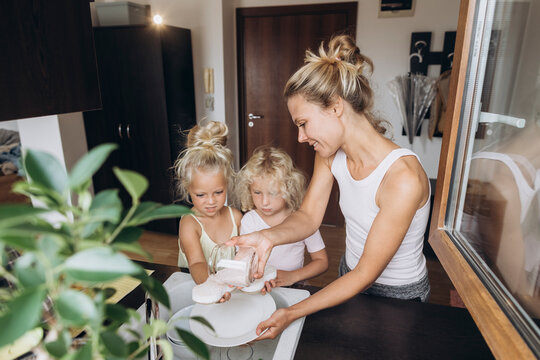 Woman with daughters washing dishes with salt in the kitchen