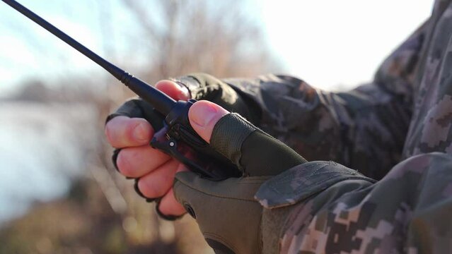 a military man in a camouflage uniform and tactical gloves adjusts a walkie-talkie to communicate with units Secure communication of the Ukrainian army during the war. encryption of radio broadcasts