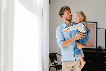 Young father holding his little daughter in hands while walking at home