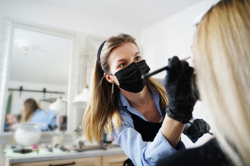 Blond beautician applying make-up on customer's face in salon