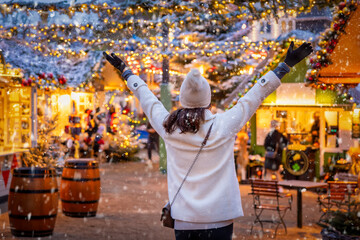 A happy tourist woman stands on a christmas market in Copenhagen, Denmark, with snow and illuminated decorations during winter time - obrazy, fototapety, plakaty