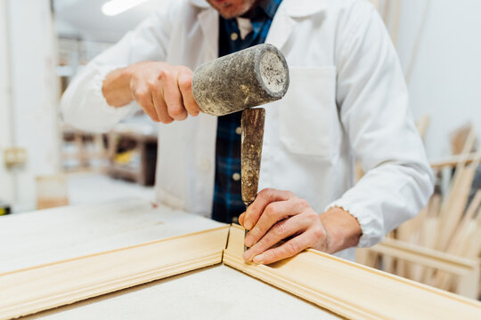 Hands of craftsman using work tool to make frame in workshop