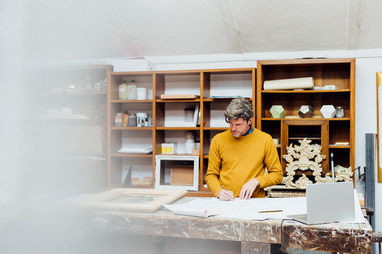 Mature craftsman sketching standing at workbench in workshop