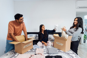 Happy women and man homepacking boxes of clothes for donation on bed at home